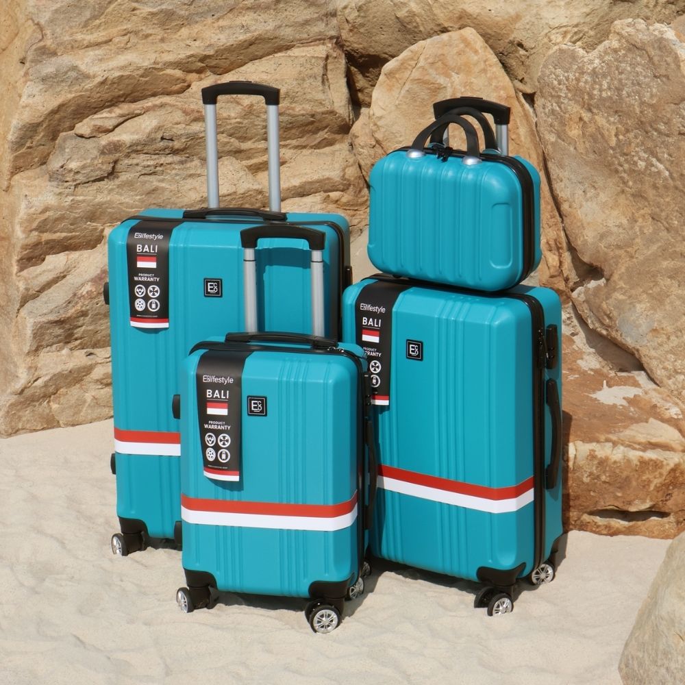 Lifestyle image of the Bali hardshell luggage set positioned on sand in front of coastal rocks, highlighting its clean design, durable build, and stylish presence in a relaxed beach setting
