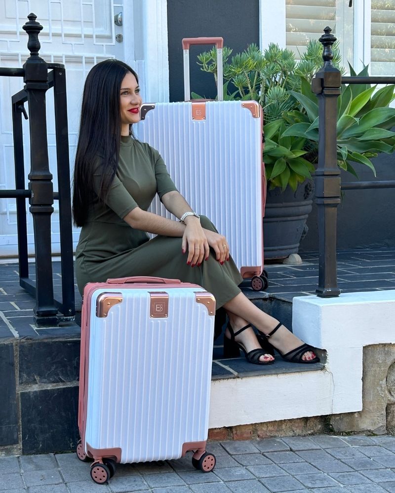 Lifestyle image of a woman sitting outside a house with the Berlin luggage set beside her, waiting for a taxi, highlighting the collection’s structured elegance, practical design, and readiness for spontaneous city departures