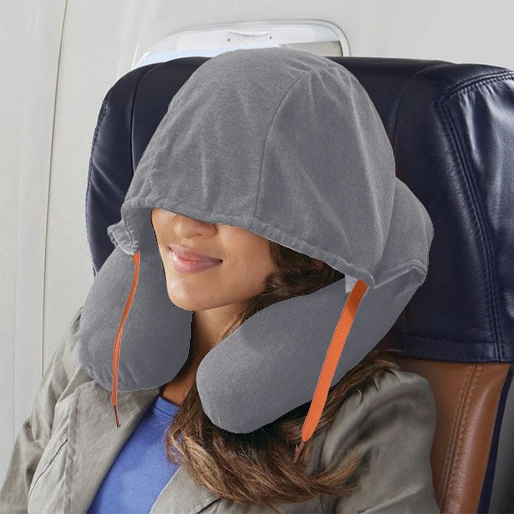Lifestyle image of a grey hooded neck pillow worn by a woman sleeping on a plane, highlighting its cozy ergonomic design and built-in hood for in-flight comfort and rest