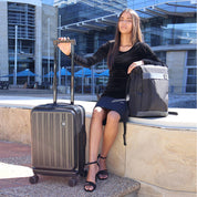 Lifestyle image of the Seattle hardshell luggage set beside a hotel entrance, with a traveler reaching for the handle—capturing its effortless mobility, sleek structure, and elevated presence in a premium travel moment